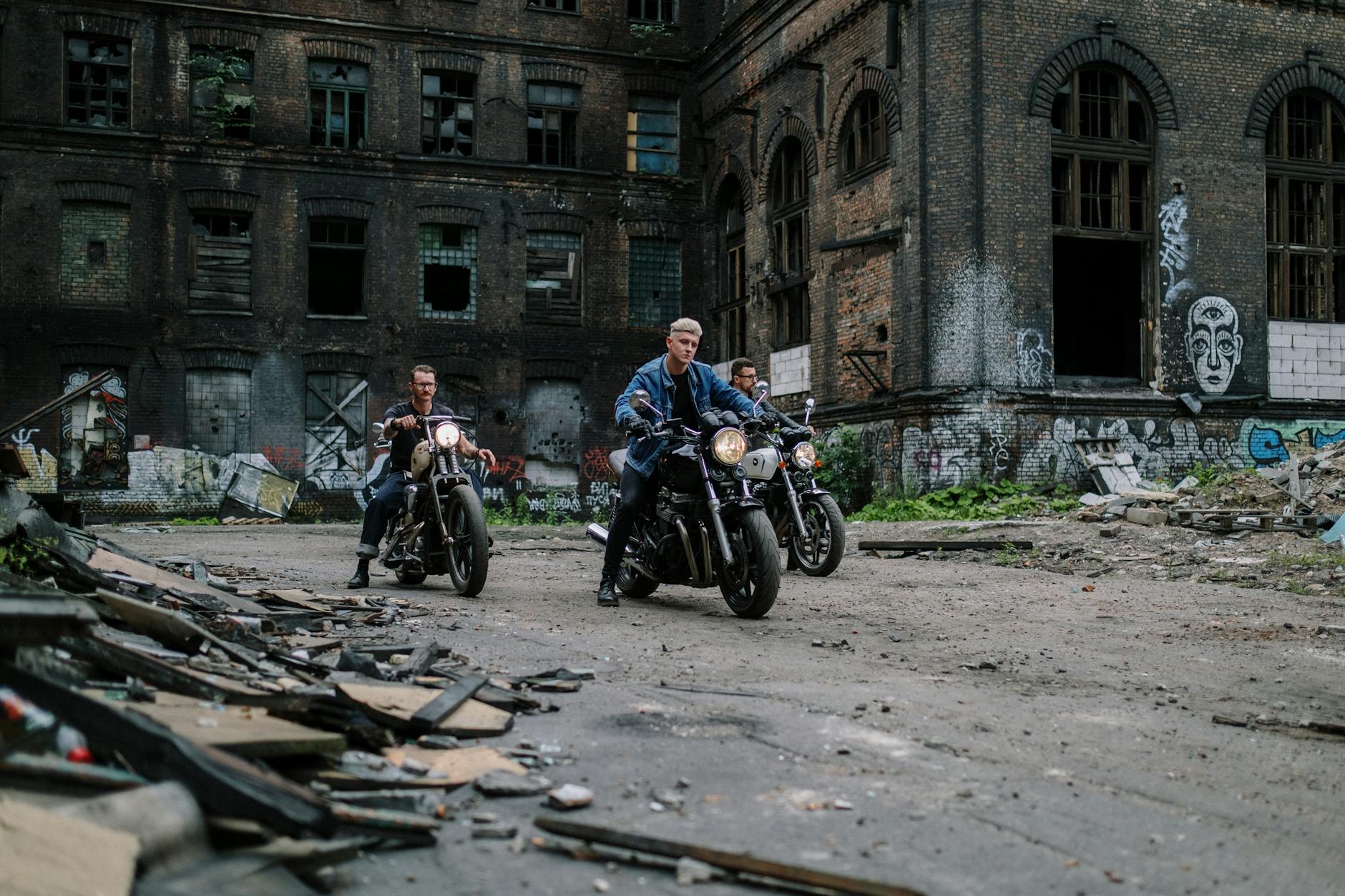 Grupa motocyklistów jedzie obok opuszczonego budynku z graffiti